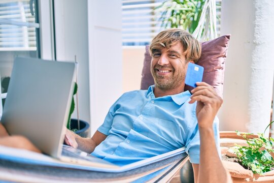 Middle age handsome man at the terrace of his house relaxing lying on a hammock doing online shopping with credit card