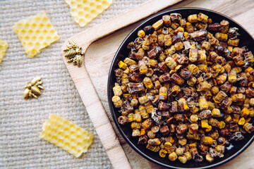 Alternative medicine bee bread ( fermented flower and plant pollen by honey bees) pellets on plate. Beeswax cera alba and bee figurines for decoration vintage jute cloth.