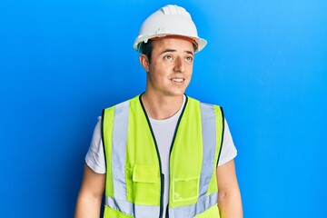 Handsome young man wearing safety helmet and reflective jacket looking away to side with smile on face, natural expression. laughing confident.