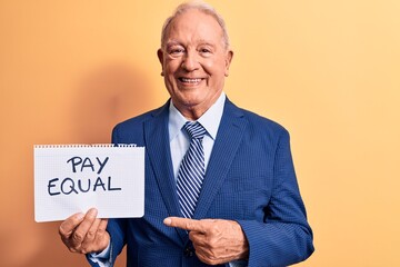 Senior handsome grey-haired businessman wearing suit holding paper with pay equal message smiling happy pointing with hand and finger