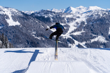 Snowboarder sliding on a rail in a snowpark in Austria on a sunny day
