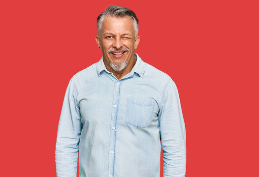 Middle age grey-haired man wearing casual clothes winking looking at the camera with sexy expression, cheerful and happy face.