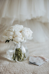 Wedding bouquet of peonies flowers in a vase stands on the bed of the newlyweds with invitations