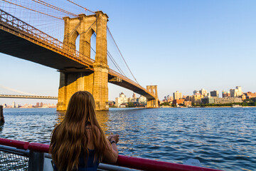 Young woman with long red hair watching the Brooklyn Bridge from Manhattan on a summer day