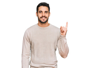 Young hispanic man wearing casual clothes with a big smile on face, pointing with hand and finger to the side looking at the camera.