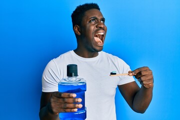 Handsome black man holding mouthwash and toothbrush for fresh breath angry and mad screaming...