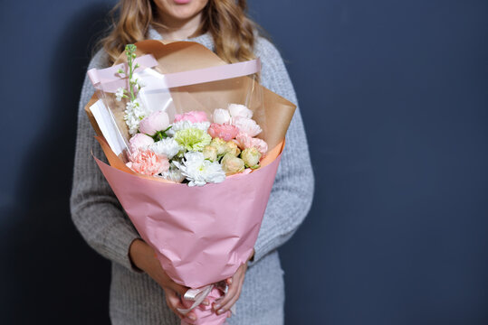 happy young blonde girl in a light gray sweater holds a bouquet of flowers in her hands on a dark gray monochrome background.