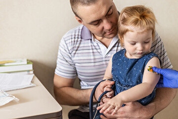 Vaccination of a little girl in her dad's arms in the doctor's office from the coronavirus....