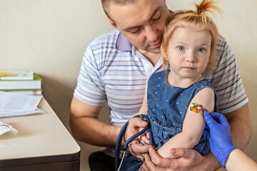 A little girl with her father in the doctor's office at the clinic is being vaccinated against the...