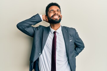 Handsome hispanic man with beard wearing business suit and tie suffering of neck ache injury, touching neck with hand, muscular pain