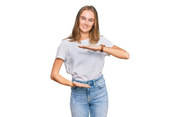 Beautiful young blonde woman wearing casual white t shirt gesturing with hands showing big and large size sign, measure symbol. smiling looking at the camera. measuring concept.