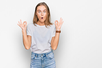 Fototapeta na wymiar Beautiful young blonde woman wearing casual white t shirt looking surprised and shocked doing ok approval symbol with fingers. crazy expression