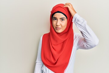 Young beautiful hispanic girl wearing traditional islamic hijab scarf confuse and wonder about question. uncertain with doubt, thinking with hand on head. pensive concept.