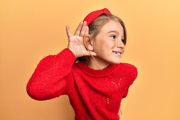 Little beautiful girl wearing casual winter sweater smiling with hand over ear listening and hearing to rumor or gossip. deafness concept.