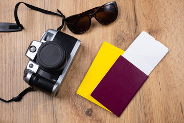The concept of new normal conditions of tourism. On the wooden table are photo camera, sunglasses, passport, international certificate of vaccination, flying ticket. Top view. Ready for safe tour