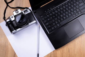 Wooden table background with open laptop near white empty sheet for your notice and vintage photo...