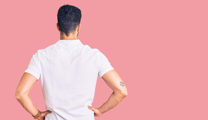 Young handsome hispanic man wearing casual clothes standing backwards looking away with arms on body