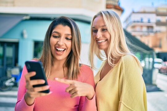 Two beautiful and young girl friends together having fun at the city using smartphone