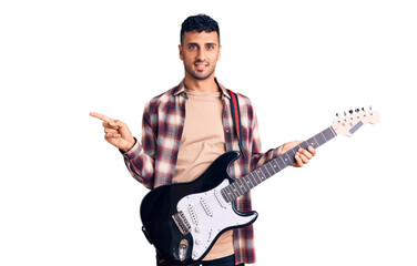 Young hispanic man playing electric guitar smiling happy pointing with hand and finger to the side
