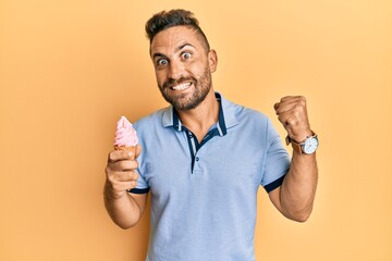 Handsome man with beard eating ice cream cone screaming proud, celebrating victory and success very...