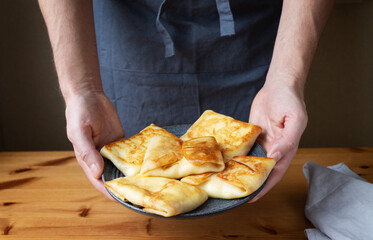 A man in the kitchen prepares a healthy breakfast of pancakes stuffed with fresh cottage cheese with sour cream and delicious fragrant honey.