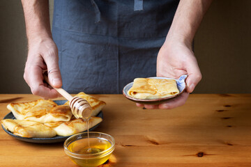 A man in the kitchen prepares a healthy breakfast of pancakes stuffed with fresh cottage cheese with sour cream and delicious fragrant honey.