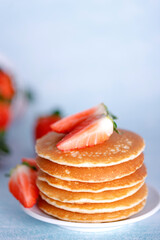 Tasty American pancakes with strawberries on white plate against blue background.