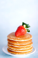 Tasty American pancakes with strawberries on white plate against blue background.