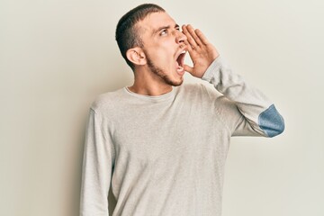 Hispanic young man wearing casual winter sweater shouting and screaming loud to side with hand on mouth. communication concept.