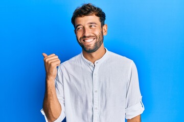 Handsome man with beard wearing elegant shirt pointing thumb up to the side smiling happy with open mouth