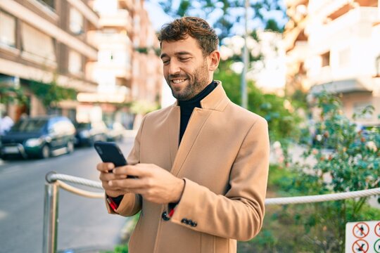 Handsome business man wearing elegant jacket using smartphone smiling happy outdoors