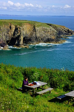 High Angle View Of Woman Sitting On Picnic Table By Sea Against Cloudy Sky