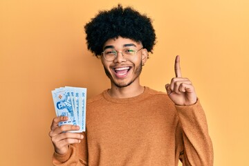 Young african american man with afro hair holding 50 thai baht banknotes smiling with an idea or...