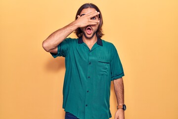 Young handsome man wearing casual clothes peeking in shock covering face and eyes with hand, looking through fingers afraid