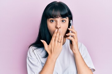Young hispanic girl having conversation talking on the smartphone covering mouth with hand, shocked and afraid for mistake. surprised expression