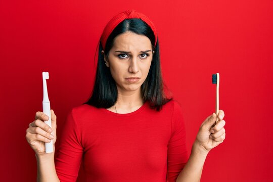 Young hispanic woman choosing electric toothbrush or normal teethbrush depressed and worry for distress, crying angry and afraid. sad expression.