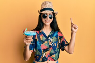 Young hispanic woman wearing summer style drinking tropical cocktail with alcohol smiling with an idea or question pointing finger with happy face, number one