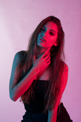 Fashion girl with long hair in a black shining dress poses in neon light in the studio