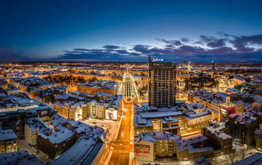 Naklejka premium Riga city panorama in winter time. Street lights glowing in blue hour. Snowy rooftops. Iconic buildings and architecture. Drone footage. 