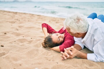 Middle age couple in love lying on the sand at the beach happy and cheerful together