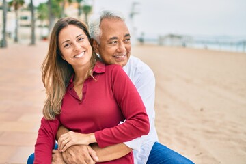 Obraz premium Middle age hispanic couple smiling happy and hugging sitting on the bench.
