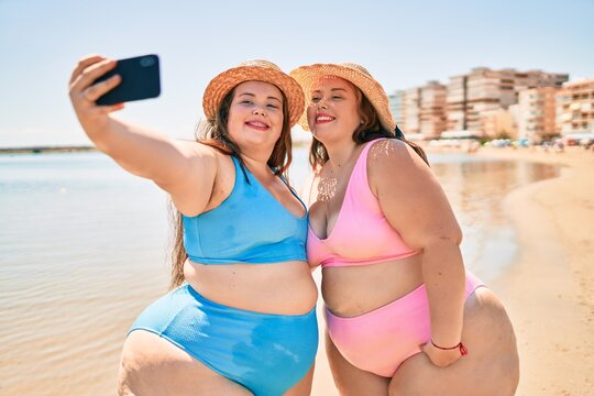 Two plus size overweight sisters twins women happy taking a selfie picture at the beach on summer holidays