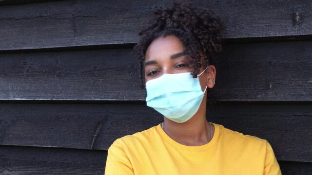 Beautiful mixed race African American girl biracial teenager teen young woman outside wearing a face mask during COVID-19 Coronavirus pandemic