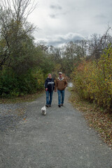 A middle-aged gay couple goes for a walk in the park with their dog in the autumn.