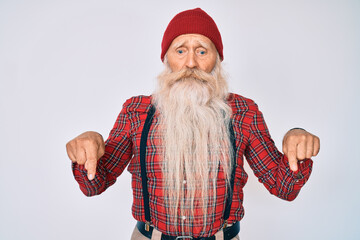 Old senior man with grey hair and long beard wearing hipster look with wool cap pointing down looking sad and upset, indicating direction with fingers, unhappy and depressed.