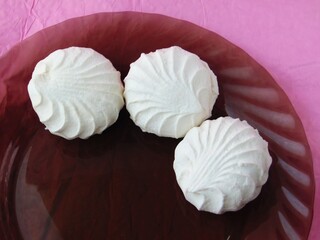 three round marshmallows are laid out in an arc on a black translucent plate on pink paper