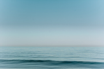 Obraz premium a smooth sea wave against the blue sky. background image of sea waves in blue tones. horizontal photo.