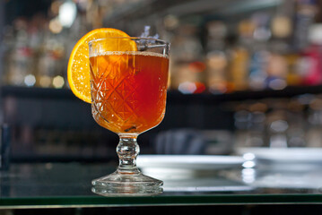 Orange cocktail on the bar. Mulled wine with white wine. Shelves with bottles of alcohol blurred in the background.