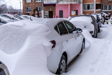 Cars in the parking lot near a residential building buried under the snow. Huge winter snowdrifts. Winter snow storm theme.