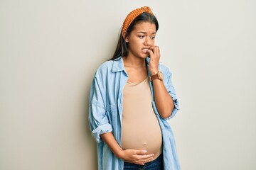 Beautiful hispanic woman expecting a baby, touching pregnant belly looking stressed and nervous...